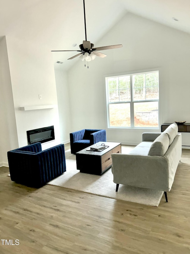 living area featuring light wood-style flooring, visible vents, high vaulted ceiling, and a glass covered fireplace