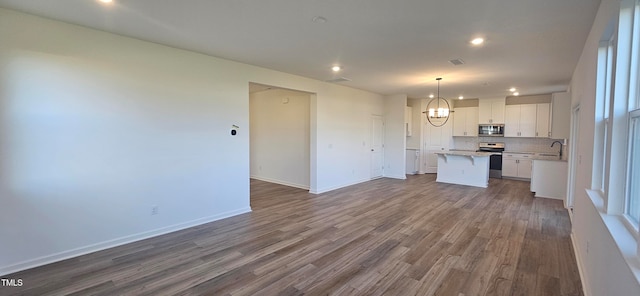 kitchen with pendant lighting, hardwood / wood-style flooring, appliances with stainless steel finishes, a kitchen island, and white cabinetry