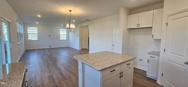 kitchen with pendant lighting, white cabinets, light stone counters, a kitchen island, and dark hardwood / wood-style flooring