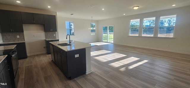 kitchen featuring black electric range, light countertops, decorative backsplash, a sink, and wood finished floors