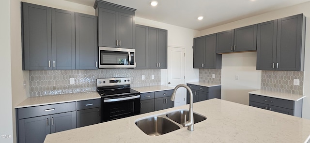 kitchen with light stone countertops, appliances with stainless steel finishes, backsplash, sink, and gray cabinets