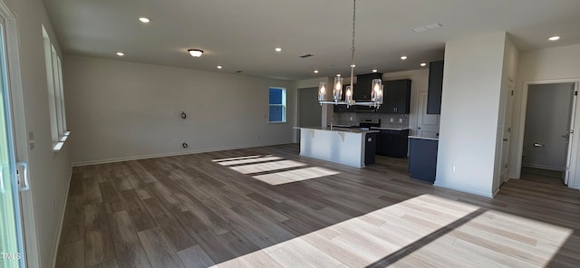 kitchen featuring open floor plan, backsplash, wood finished floors, and a kitchen island with sink