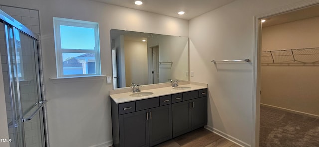 bathroom with a walk in closet, a sink, a shower stall, and baseboards