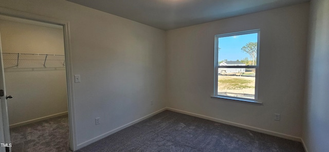 unfurnished bedroom featuring dark colored carpet, a closet, a walk in closet, and baseboards