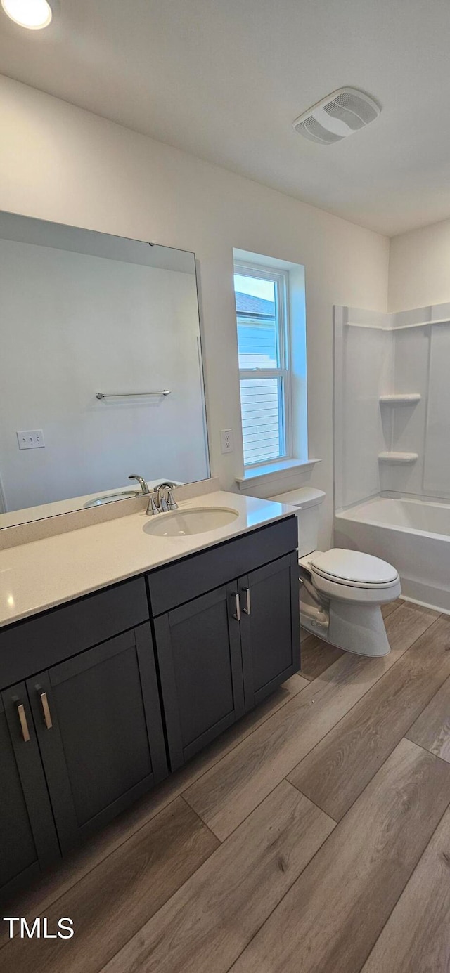 bathroom with visible vents, toilet, washtub / shower combination, vanity, and wood finished floors