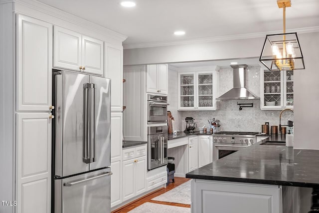 kitchen with wall chimney exhaust hood, premium appliances, white cabinetry, and sink