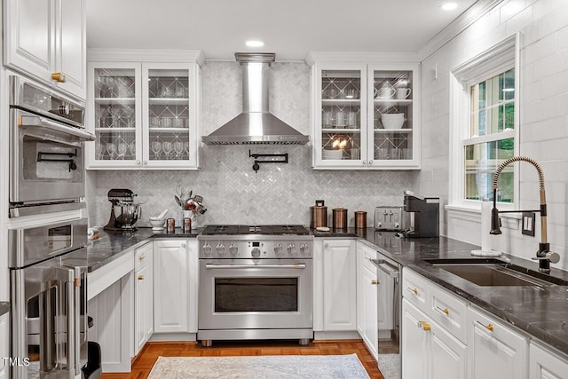 kitchen featuring white cabinets, stainless steel appliances, wall chimney exhaust hood, and sink