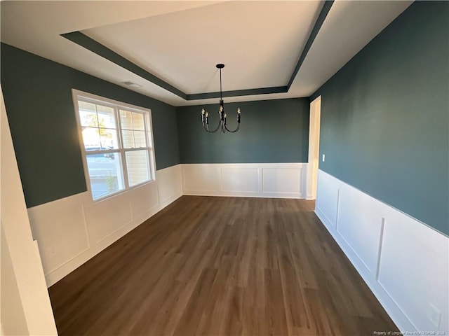 unfurnished dining area featuring a tray ceiling, dark hardwood / wood-style floors, and an inviting chandelier