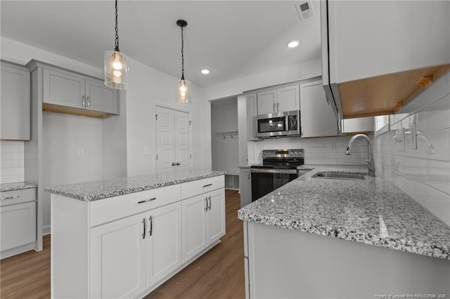 kitchen with hanging light fixtures, a kitchen island, sink, wood-type flooring, and appliances with stainless steel finishes