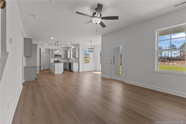 unfurnished living room featuring ceiling fan with notable chandelier and dark wood-type flooring