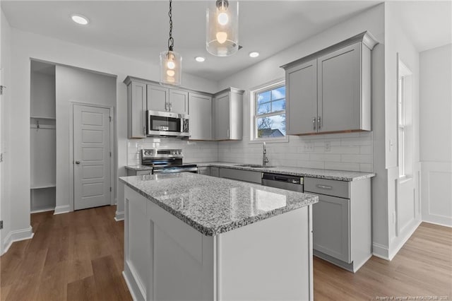 kitchen with stainless steel appliances, a kitchen island, light stone countertops, sink, and gray cabinets