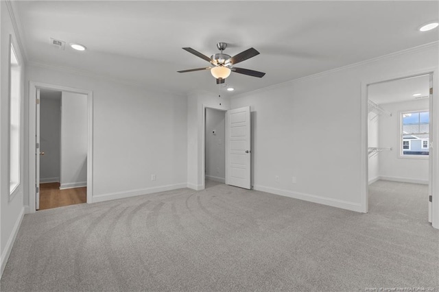 unfurnished bedroom with ornamental molding, a spacious closet, and light carpet