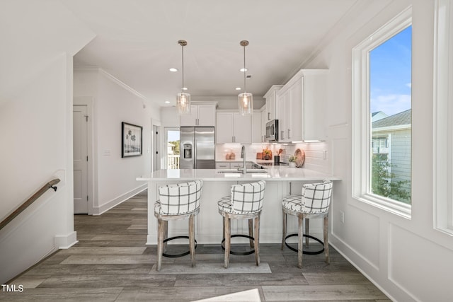 kitchen featuring appliances with stainless steel finishes, pendant lighting, a breakfast bar area, white cabinets, and ornamental molding