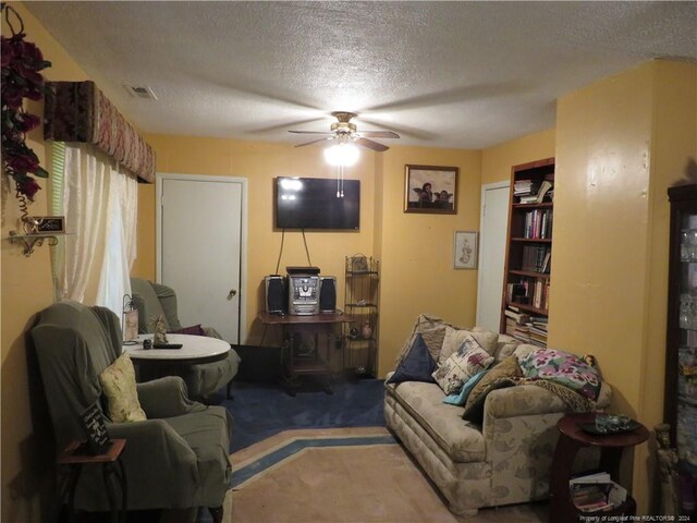 living room with ceiling fan, carpet floors, and a textured ceiling