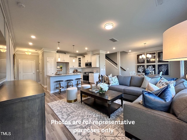 living room with wood-type flooring, ornamental molding, and a notable chandelier