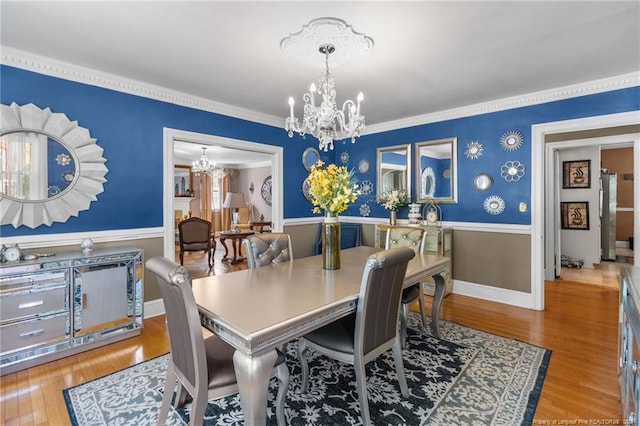 dining room featuring wood-type flooring, ornamental molding, and a notable chandelier