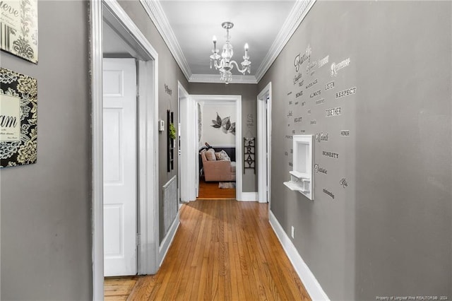 hall with light wood-type flooring, an inviting chandelier, and crown molding