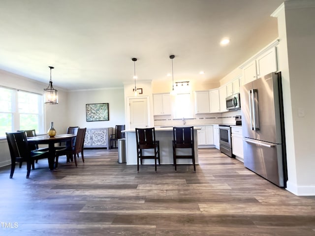 kitchen with hanging light fixtures, stainless steel appliances, a kitchen island, a kitchen breakfast bar, and white cabinets