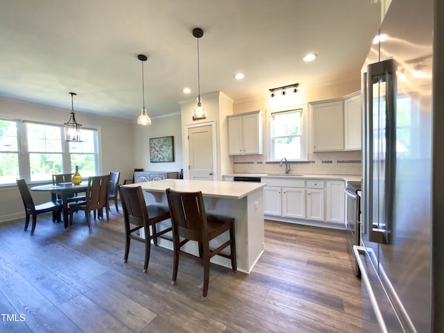 kitchen featuring white cabinetry, a center island, stainless steel appliances, decorative light fixtures, and a breakfast bar area