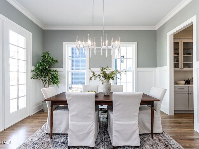 dining room with wainscoting, crown molding, an inviting chandelier, and wood finished floors