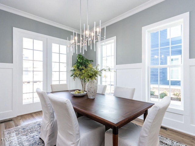 dining area featuring visible vents, a decorative wall, ornamental molding, wainscoting, and wood finished floors