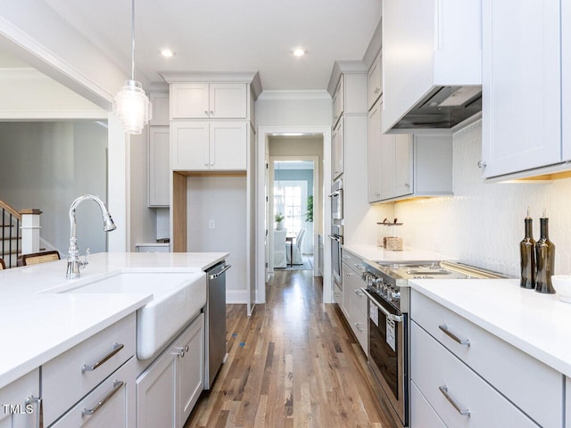 kitchen featuring light wood-style flooring, stainless steel appliances, light countertops, wall chimney range hood, and decorative light fixtures