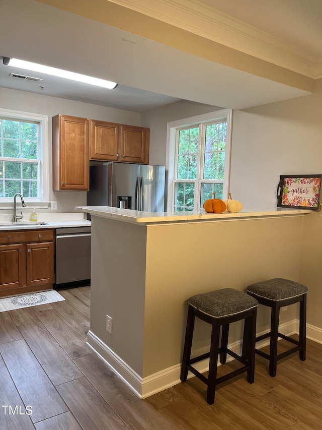 kitchen with a breakfast bar, crown molding, sink, appliances with stainless steel finishes, and wood-type flooring