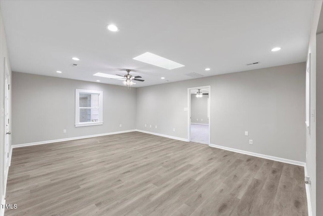 empty room featuring ceiling fan, a skylight, and light wood-type flooring