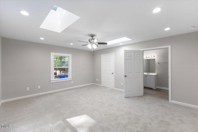 unfurnished bedroom with light carpet, connected bathroom, and a skylight