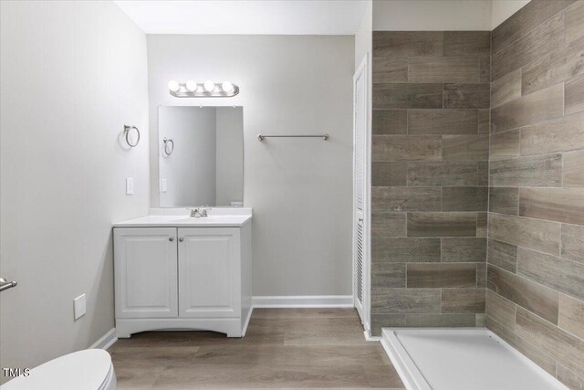 bathroom featuring wood-type flooring, toilet, a tile shower, and vanity