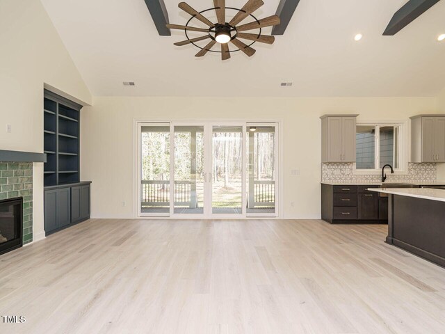 unfurnished living room featuring sink, a fireplace, vaulted ceiling, ceiling fan, and light hardwood / wood-style flooring