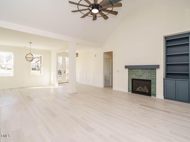 unfurnished living room with light wood-type flooring, a towering ceiling, built in shelves, a fireplace, and ceiling fan with notable chandelier