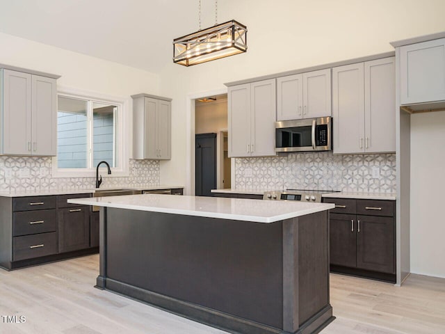 kitchen with sink, a center island, light hardwood / wood-style floors, hanging light fixtures, and gray cabinetry