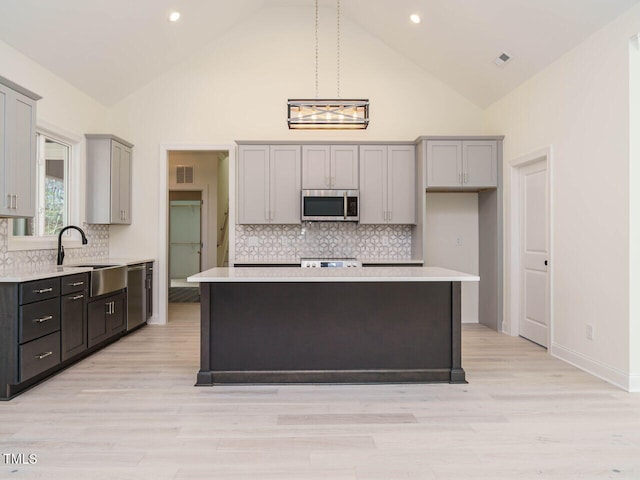 kitchen with appliances with stainless steel finishes, gray cabinetry, a center island, high vaulted ceiling, and decorative backsplash