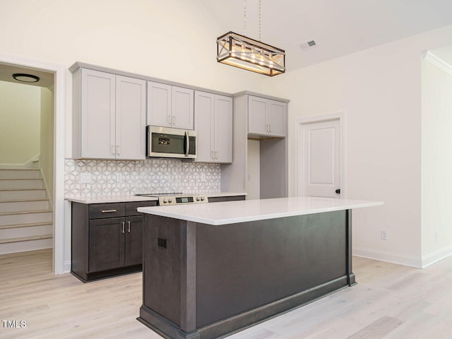 kitchen with pendant lighting, a center island, light wood-type flooring, backsplash, and gray cabinetry