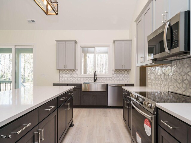 kitchen featuring stainless steel appliances, tasteful backsplash, light wood-type flooring, gray cabinets, and sink