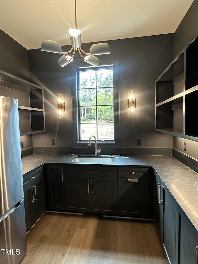 kitchen with a sink, dark cabinets, freestanding refrigerator, wood finished floors, and open shelves