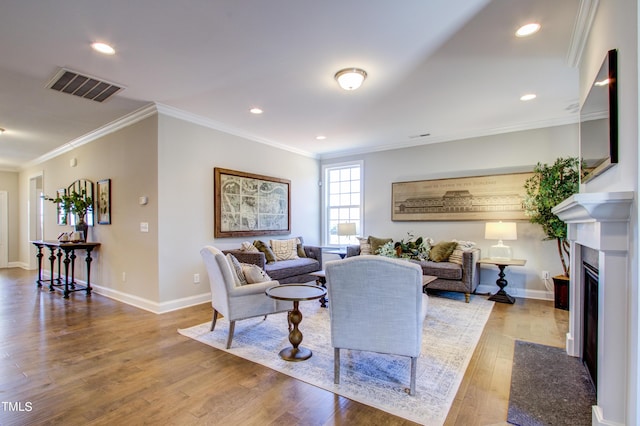 living room with crown molding, baseboards, visible vents, a fireplace with flush hearth, and light wood-type flooring