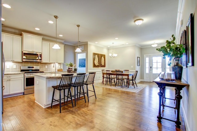 kitchen featuring a kitchen island with sink, hanging light fixtures, white cabinets, and stainless steel appliances