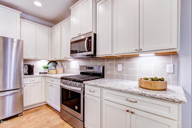 kitchen featuring light stone counters, white cabinets, decorative backsplash, and stainless steel appliances