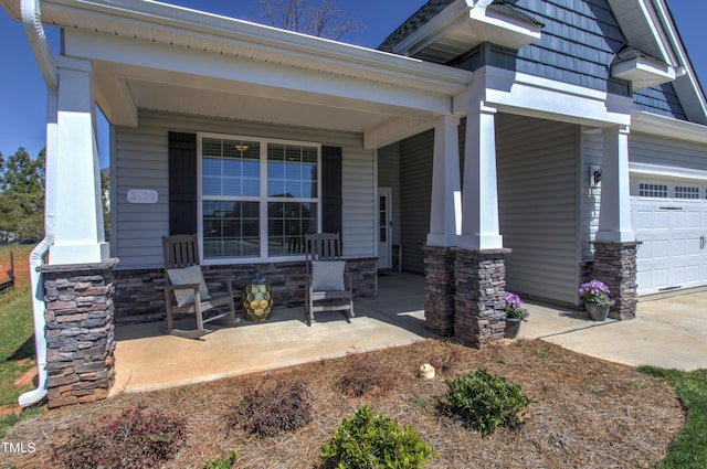 view of exterior entry featuring an attached garage, stone siding, and covered porch