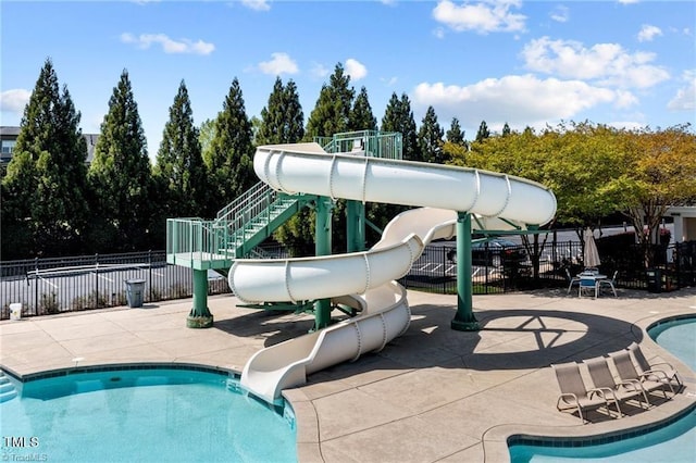 community pool featuring playground community, a water slide, a patio area, and fence