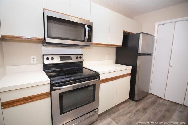 kitchen with hardwood / wood-style floors, stainless steel appliances, and white cabinetry