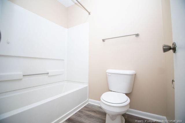 bathroom featuring hardwood / wood-style floors, washtub / shower combination, and toilet