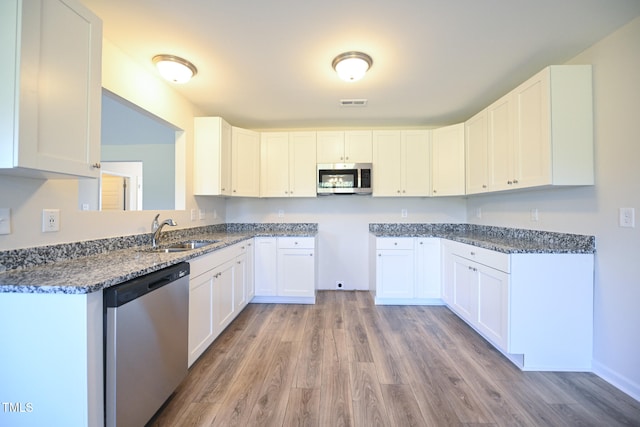 kitchen featuring appliances with stainless steel finishes, white cabinetry, sink, dark stone countertops, and light wood-type flooring