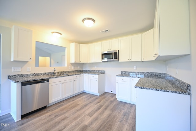 kitchen with sink, white cabinetry, dark stone countertops, stainless steel appliances, and light wood-type flooring