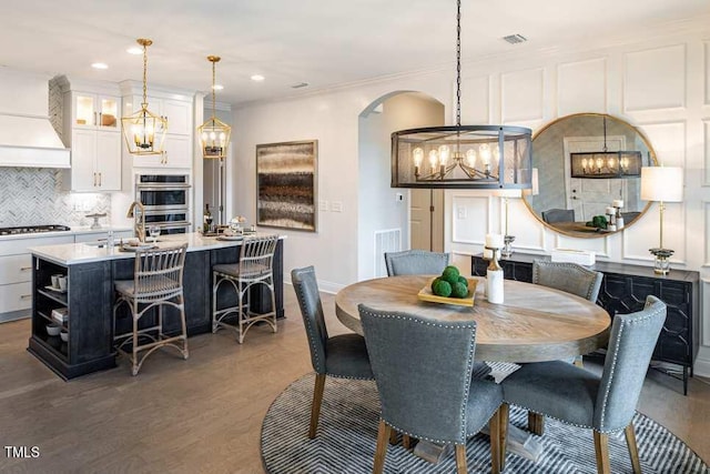 dining area with ornamental molding, dark wood-type flooring, sink, and a chandelier