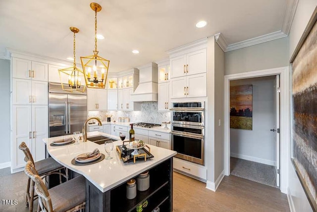 kitchen featuring sink, custom exhaust hood, a center island with sink, stainless steel appliances, and white cabinets