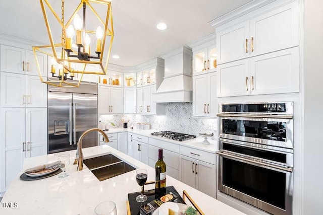 kitchen with sink, white cabinets, hanging light fixtures, stainless steel appliances, and custom range hood