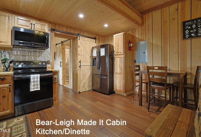 kitchen featuring stainless steel appliances, beam ceiling, a barn door, wood walls, and hardwood / wood-style flooring